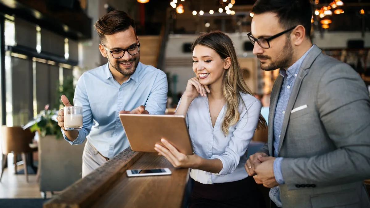 Trzy osoby rozmawiają i uśmiechają się podczas spotkania w pracy, oglądając table