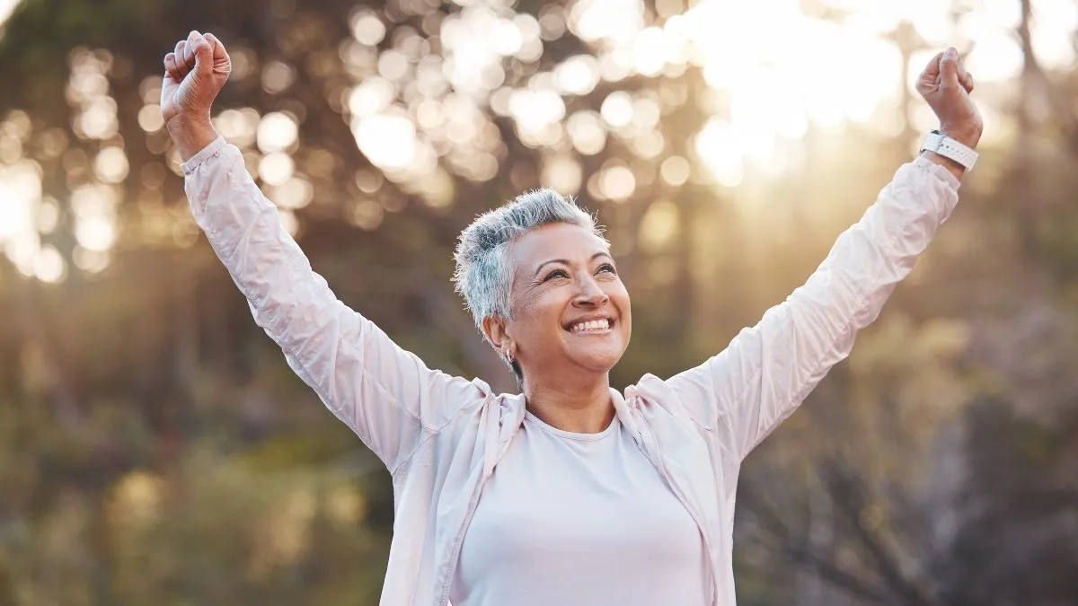 Uśmiechnięta kobieta z uniesionymi rękami, symbol odzyskiwania siły, radości i motywacji do życia.