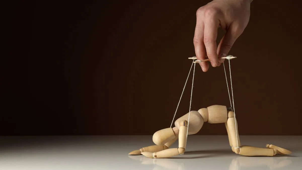 Figurka marionetki w pozycji uległości sterowana ręką – metafora relacji z narcyzem i utraty wolnej woli